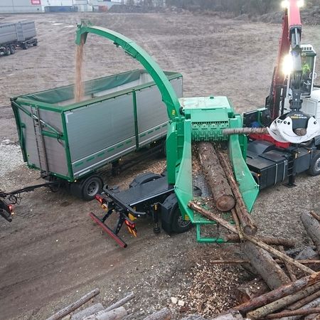 Ein Lkw lädt Holzstämme auf einen Anhänger, während die Umgebung von Bäumen umgeben ist.