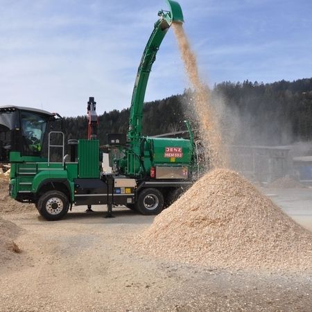 Eine grüne Maschine kippt Holzspäne in einen Haufen.