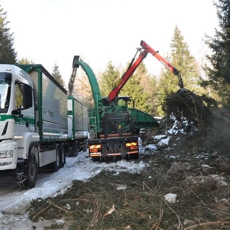 Ein Lastwagen bewegt sich auf einer schneebedeckten Straße, umgeben von einer winterlichen Szenerie.
