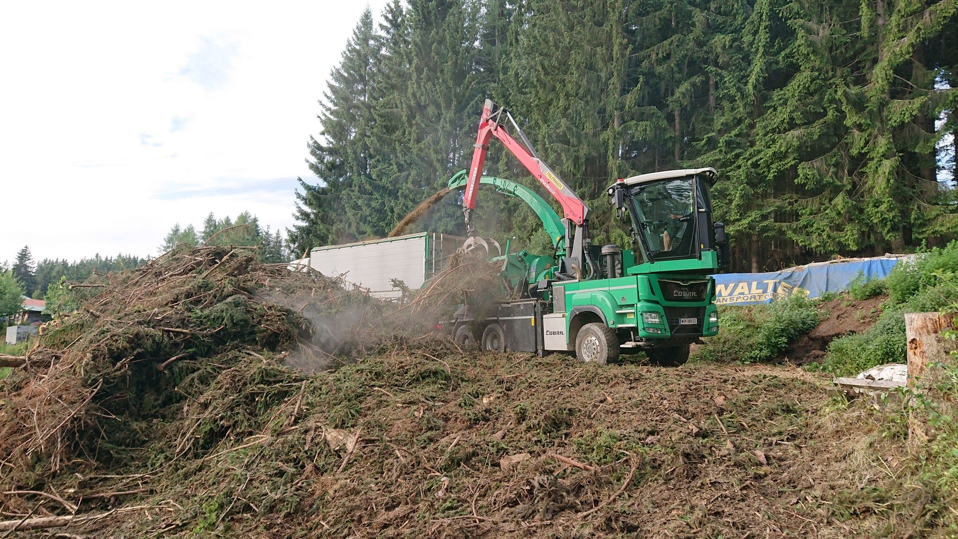 Eine grüne Maschine bearbeitet einen Holzstapel auf einem Baustellengelände.